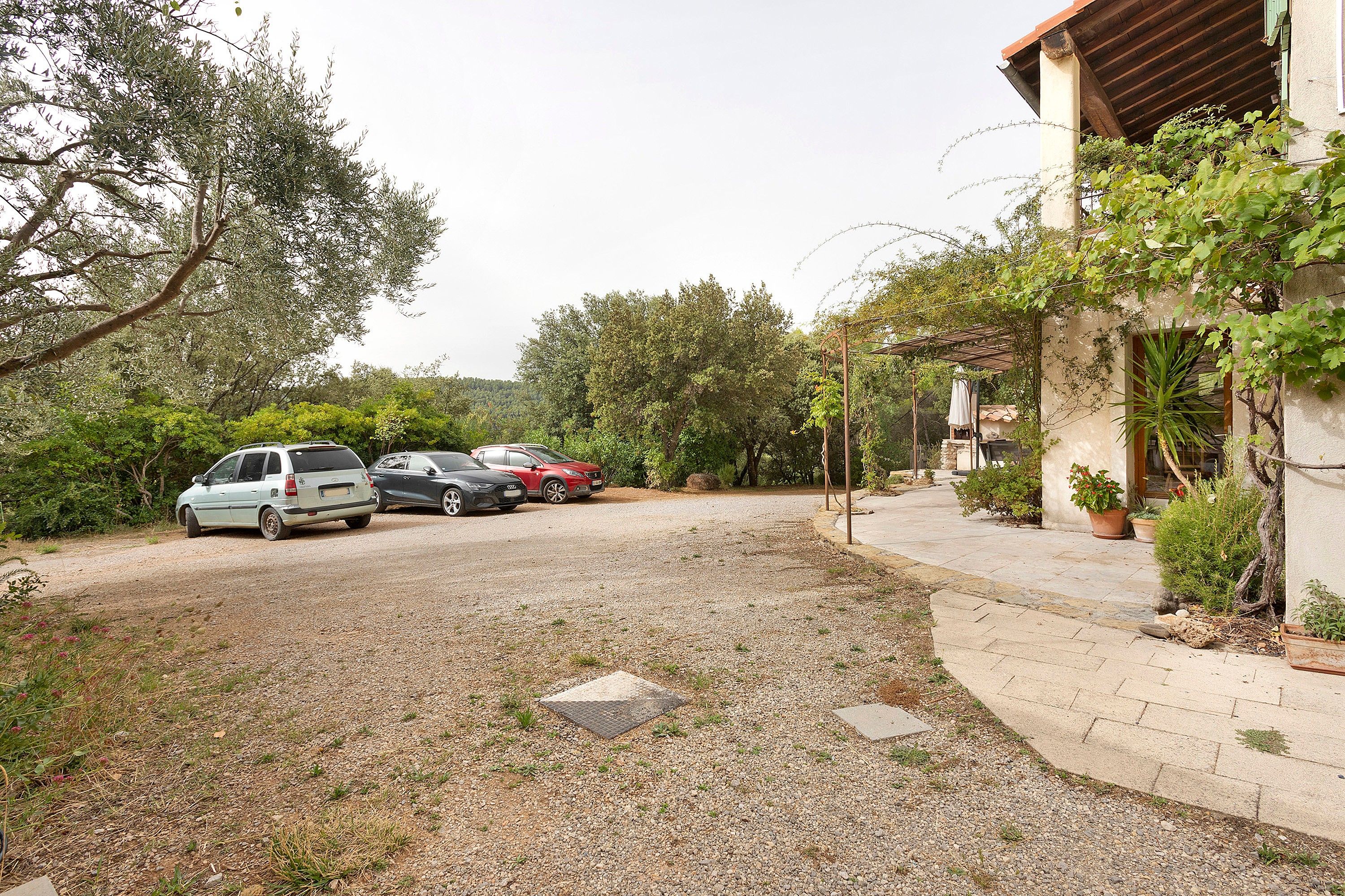 A gravel driveway with parked cars and a house with a garden.