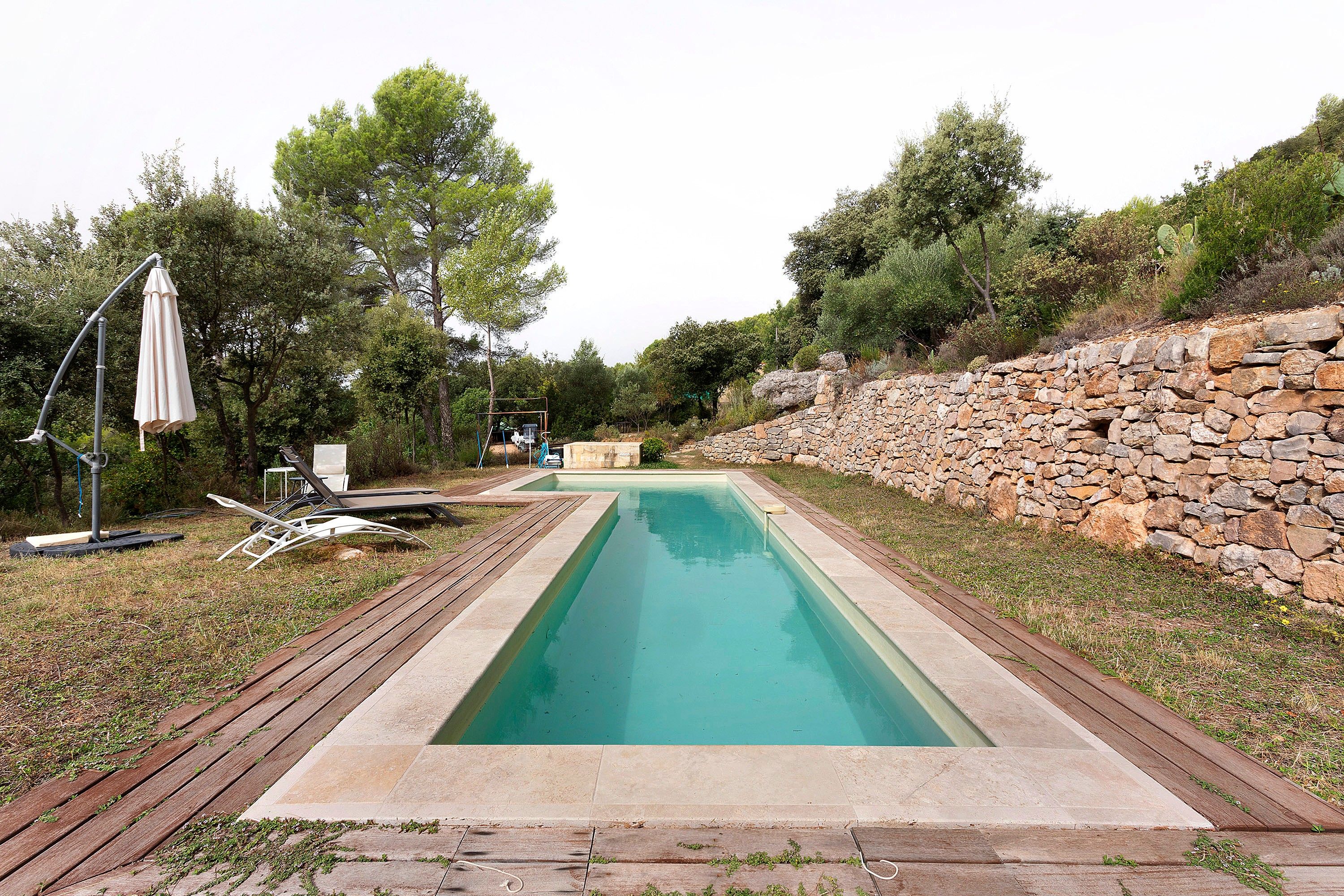 Una piscina rectangular con un muro de piedra en un lado y una terraza de madera en el otro.