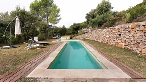 A rectangular swimming pool with a stone wall on one side and a wooden deck on the other.