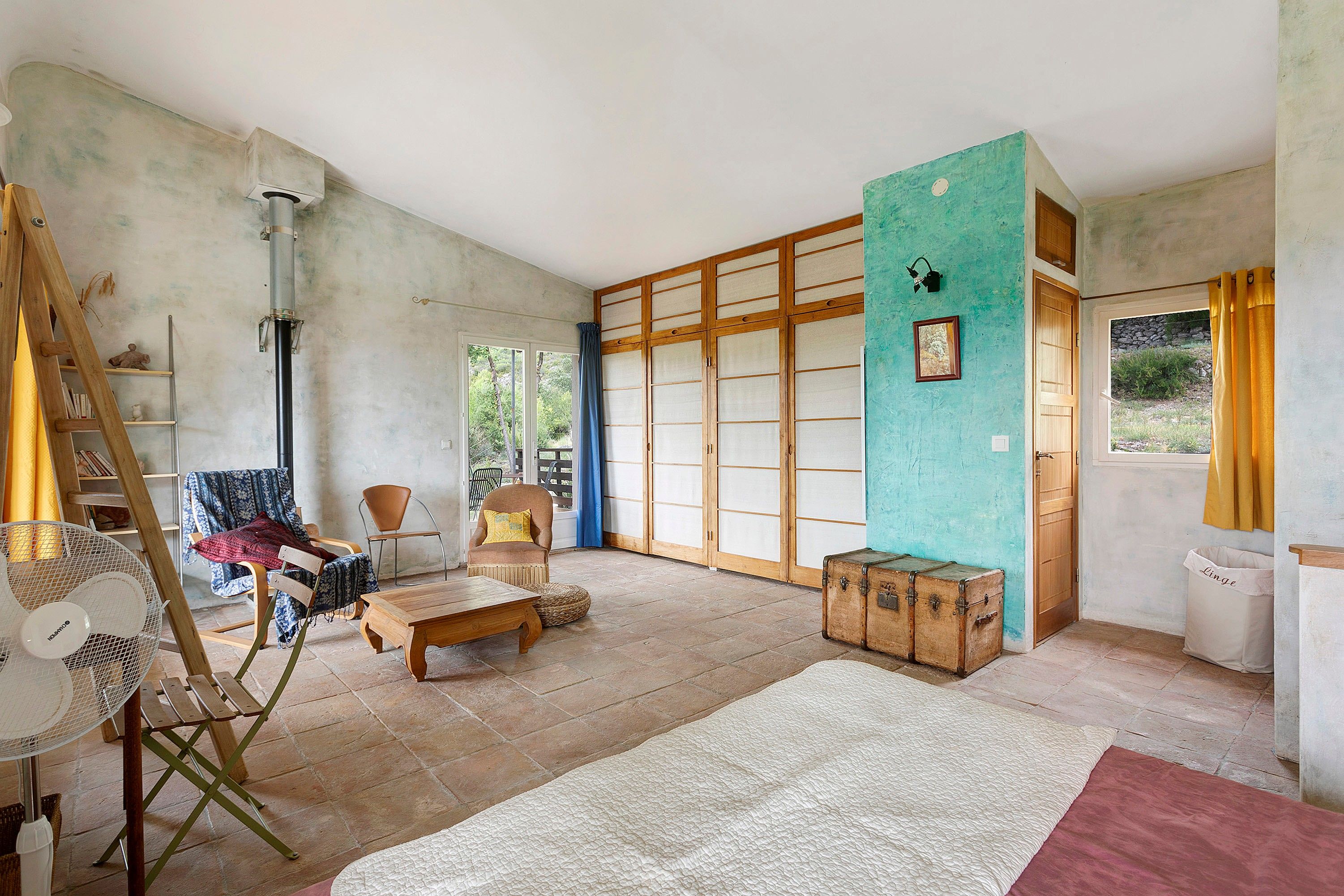 A spacious room with a large sliding door, a wooden bench, a fan, and a suitcase.