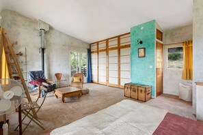 Una habitación amplia con un gran ventanal corredera, un banco de madera, un ventilador y una maleta.