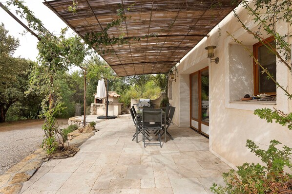 Un patio al aire libre con una pérgola, suelo de piedra y una mesa de comedor con sillas.