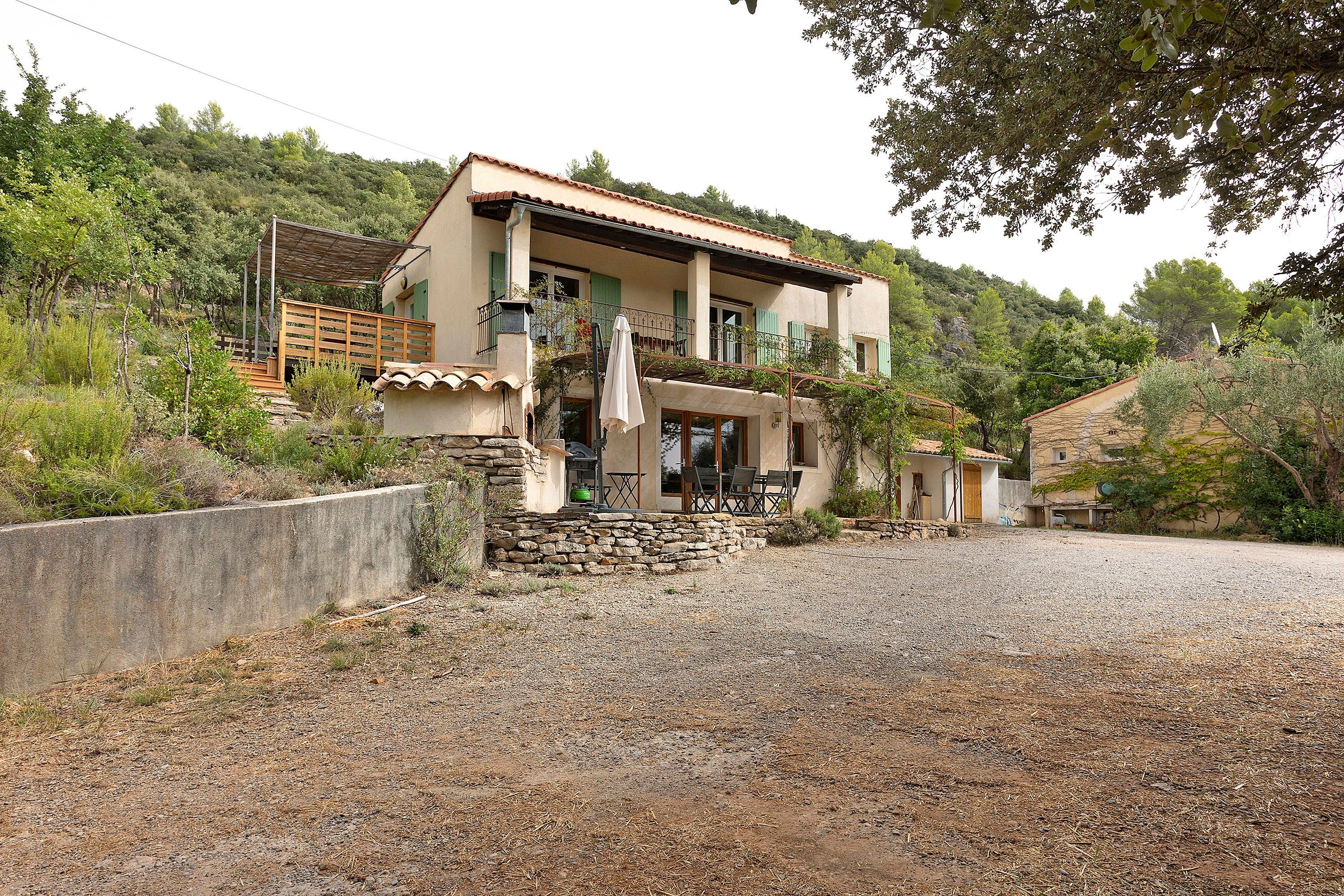 A two-story house with a stone staircase leading to the entrance, a balcony with a metal railing, and a gravel driveway.
