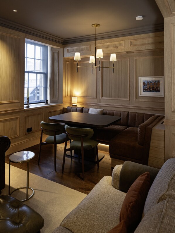 A dining area with a wooden paneled wall, a chandelier, a table with chairs, and a sofa. - Market Street (No 85B) | St Andrews (St Andrews)
