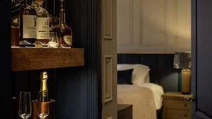 Habitació d'hotel amb nevera, un llit, una tauleta de nit i una porta que dona a una altra habitació.