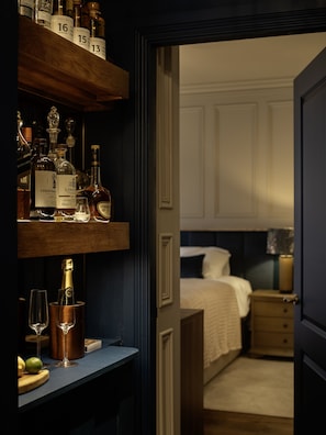 Ein Hotelzimmer mit Minibar, einem Bett, einem Nachttisch und einer Tür zu einem weiteren Raum.