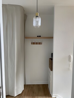 Un couloir doté d’un plancher en bois, d’une suspension lumineuse, d’un meuble à chaussures et d’un mur blanc muni d’une prise téléphonique.