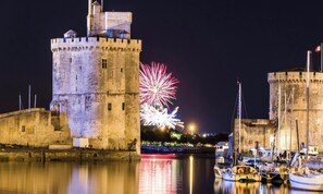 Une tour de pierre historique se dresse au bord d’un plan d’eau paisible, où des bateaux sont amarrés à proximité.