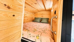 A small, wooden cabin-style room with a bed, green pillows, and a metal handle on the door. - Cowboy Trailer - Unique Tiny House (Mignaloux-Beauvoir)