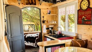 A wooden interior with a bar area, a round table, and a clock on the wall. - Cowboy Trailer - Unique Tiny House (Mignaloux-Beauvoir)