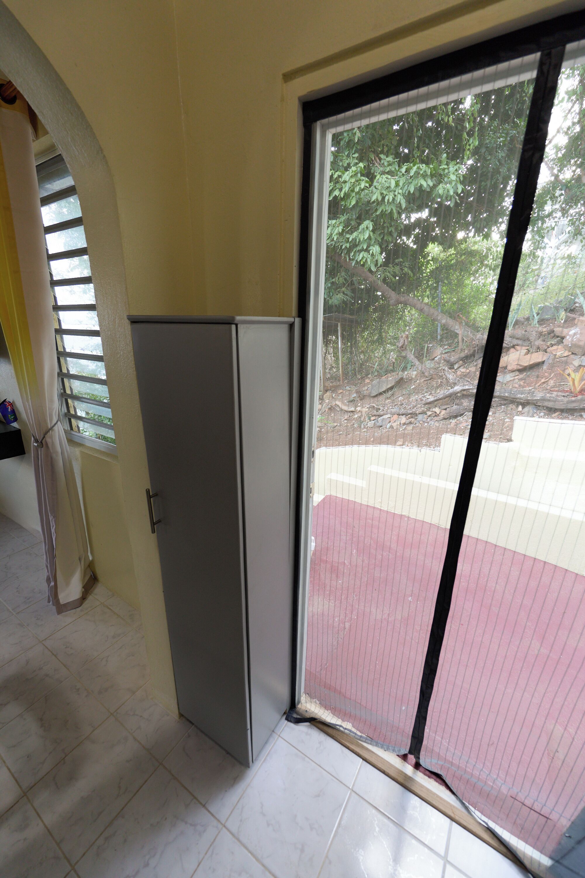 A room with a sliding glass door to a red-tiled outdoor area, a white cabinet, and a window with blinds.