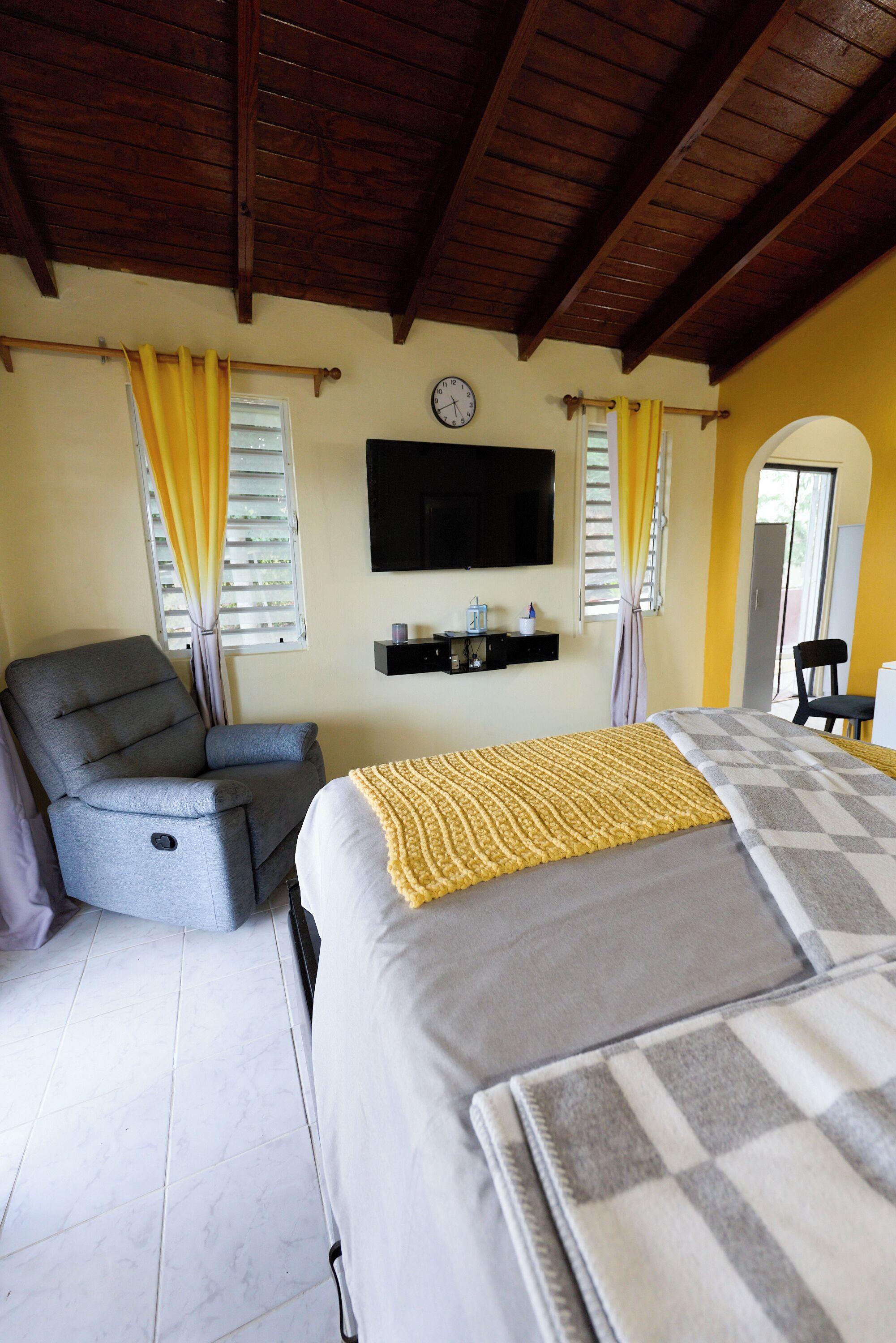 A bedroom with a bed, a chair, a TV, and a clock on the wall.