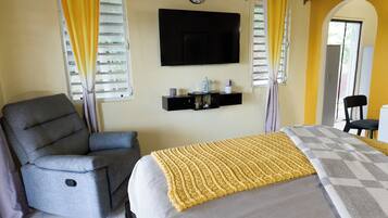 A bedroom with a bed, a chair, a TV, and a clock on the wall.