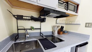 A compact kitchen with a sink, stove, microwave, and a small countertop area. - Haversville Canary Studio with stunning ocean views on Tortola, Virgin Islands (Tortola)