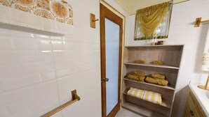 A bathroom with white tiled walls, a wooden door, a shelf with towels, and a mirror with a gold curtain. - Haversville Canary Studio with stunning ocean views on Tortola, Virgin Islands (Tortola)