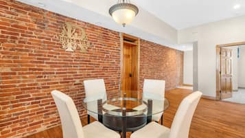 Una habitación con pared de ladrillo, una mesa redonda de cristal con cuatro sillas, una puerta de madera y una lámpara colgante.