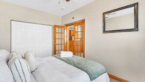 Een slaapkamer met een bed, kussens, een plafondventilator, een kledingkast, een spiegel en een deur.