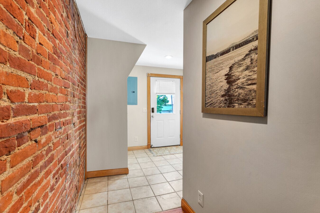 Un pasillo con pared de ladrillo, una puerta blanca y un cuadro enmarcado en la pared.