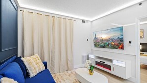 A modern living room with a blue sofa, a flat-screen TV, and a cityscape painting. - Suite c/ Vista Piscina + Parking Gratis (Orlando)