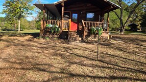 A wooden cabin with a porch, a red door, and a small garden area.