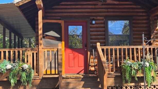 Eine Blockhütte mit roter Tür, Holzveranda und Blumentöpfen.