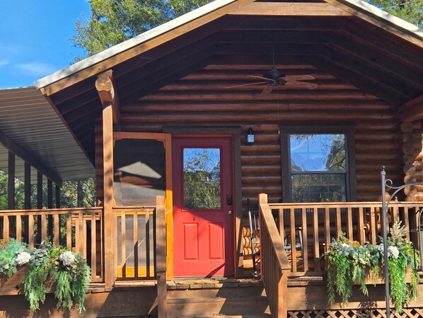 A log cabin with a red door, wooden porch, and potted plants.