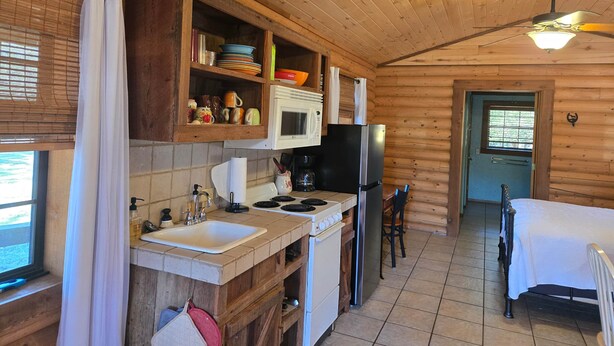 A wooden cabin kitchen with a sink, stove, refrigerator, and cabinets.