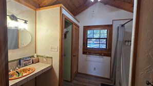 A bathroom with a wooden ceiling, a window, a sink with a colorful design, and a shower area.