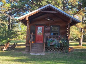 A log cabin with a red door, a porch with a railing, and a small garden area.