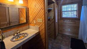 Een houten badkamer in een chalet, met een wastafel, spiegel en douche.