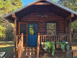 A log cabin with a blue door, a wooden porch, and a ceiling fan.