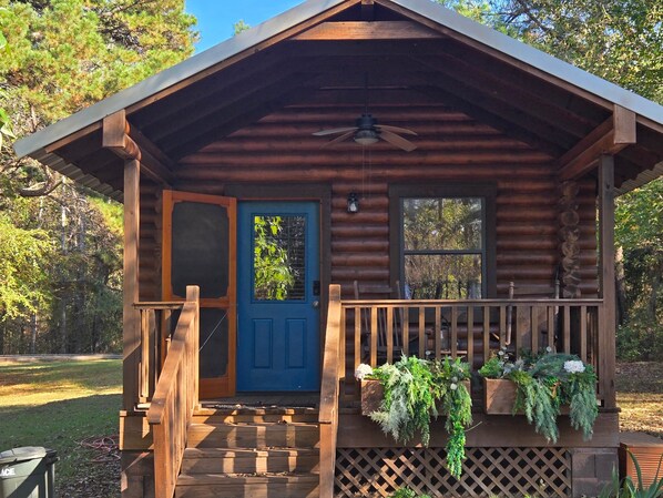 Eine Blockhütte mit blauer Tür, einer Holzterrasse und einem Deckenventilator.