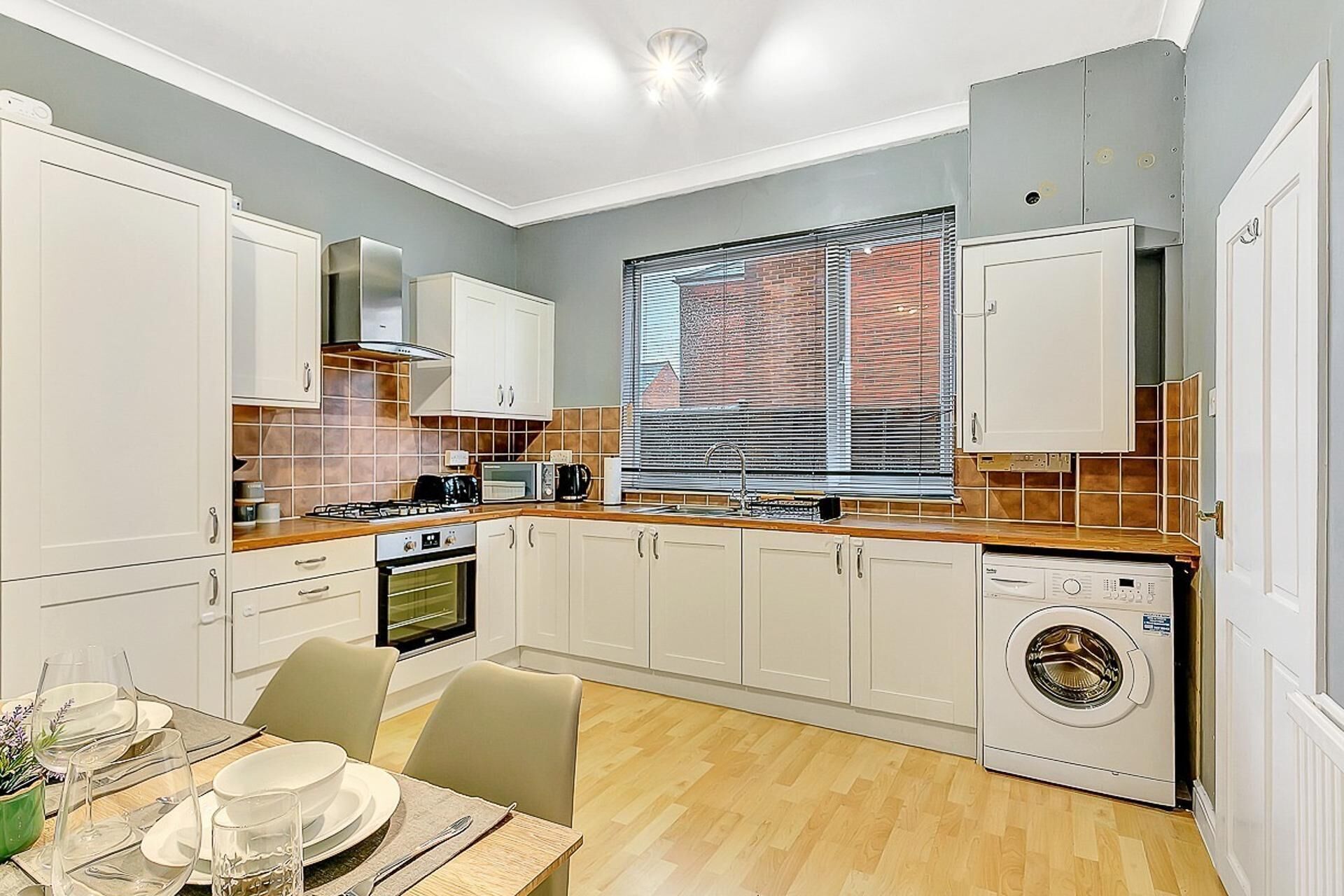 A compact kitchen with white cabinets, a built-in oven, a microwave, and a washing machine.