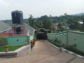 A paved pathway leading to a gated entrance, surrounded by greenery and a water tank on the left.