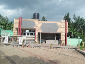 A building with a flat roof, a water tank on top, and a paved entrance area with potted plants.
