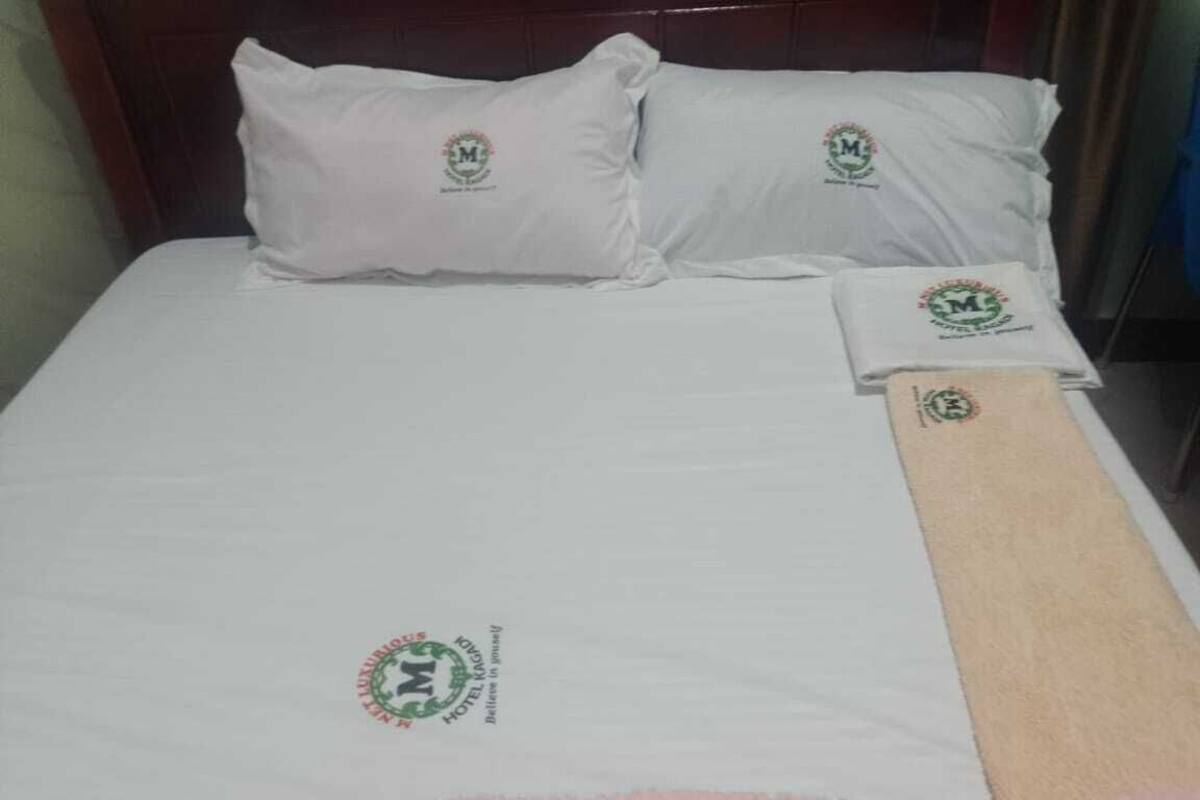 A bed with white bedding and pillows, a pink blanket, and a brown towel.