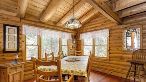 Interior de una cabaña de madera con una mesa de comedor, sillas, una araña y cuadros en las paredes.
