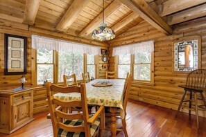 A wooden cabin interior with a dining table, chairs, a chandelier, and framed pictures on the walls. - This newer, spacious 2600 sq. ft 2-story log home is well insulated with thermostatically controlled central heating.  There are 4 large bedrooms and the Master Suite is complete with a king size brass bed with a separate sitting area, 25" Color Tele (Idyllwild Ca 92549)