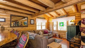 Interior de una cabaña de madera con una mesa de comedor, un sofá y un armario verde.
