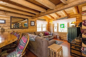 A log cabin interior with a wooden dining table, sofa, and a green cabinet. - This newer, spacious 2600 sq. ft 2-story log home is well insulated with thermostatically controlled central heating.  There are 4 large bedrooms and the Master Suite is complete with a king size brass bed with a separate sitting area, 25" Color Tele (Idyllwild Ca 92549)