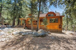 A log cabin with a wooden deck, surrounded by trees and rocks. - This newer, spacious 2600 sq. ft 2-story log home is well insulated with thermostatically controlled central heating.  There are 4 large bedrooms and the Master Suite is complete with a king size brass bed with a separate sitting area, 25" Color Tele (Idyllwild Ca 92549)