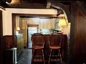 A kitchen with wooden cabinets, a refrigerator, a sink, and two wooden bar stools.