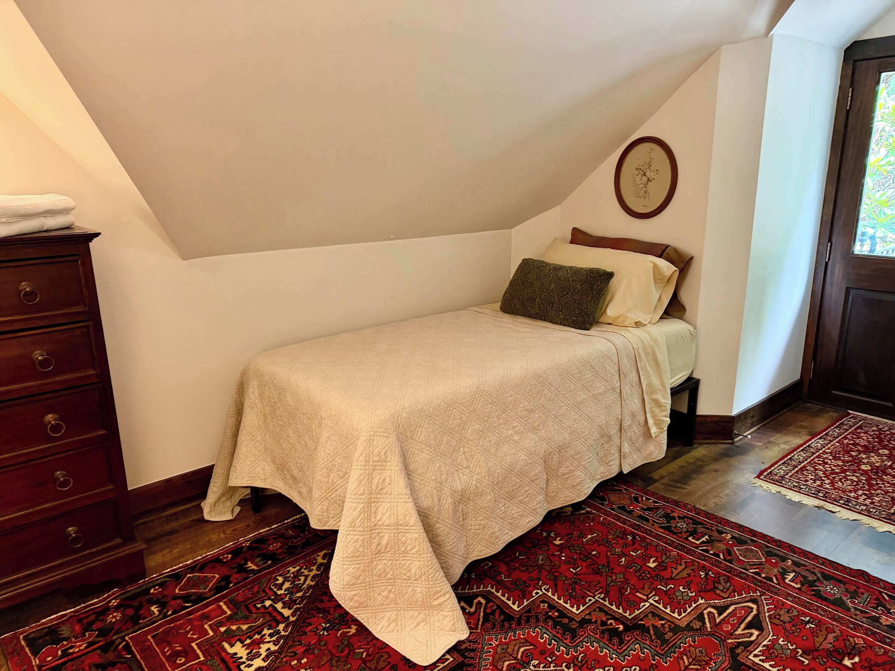 A bedroom with a bed, a dresser, a rug, and a door.