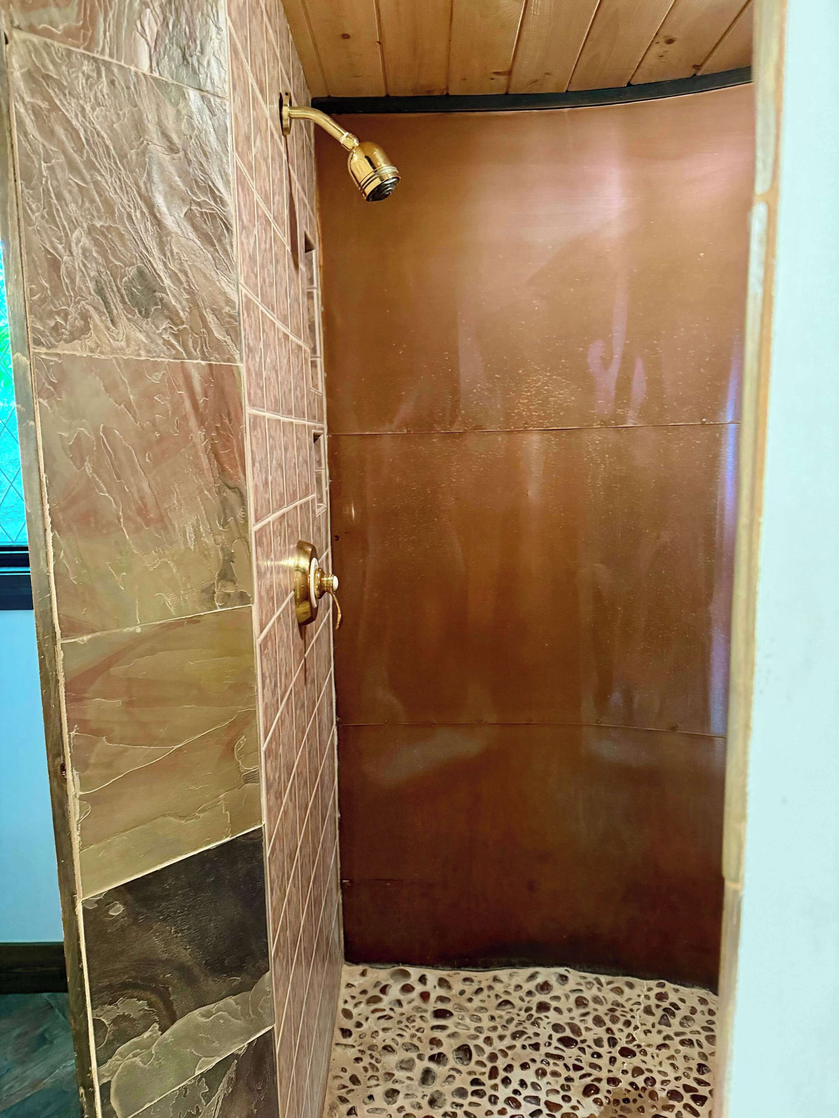 A shower with a handheld showerhead, a tiled wall, and a wooden ceiling.