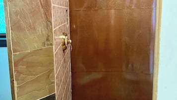 A shower with a handheld showerhead, a tiled wall, and a wooden ceiling.