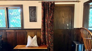 A room with a bench, a door, patterned curtains, a framed artwork, and a patterned rug.