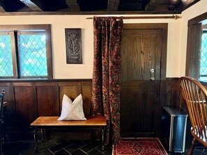 A room with a bench, a door, patterned curtains, a framed artwork, and a patterned rug.