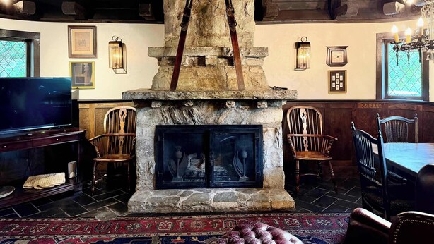 A rustic interior with a stone fireplace, wooden beams, and a dining area with chairs and a table.