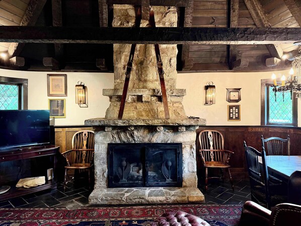 A rustic interior with a stone fireplace, wooden beams, and a dining area with chairs and a table.
