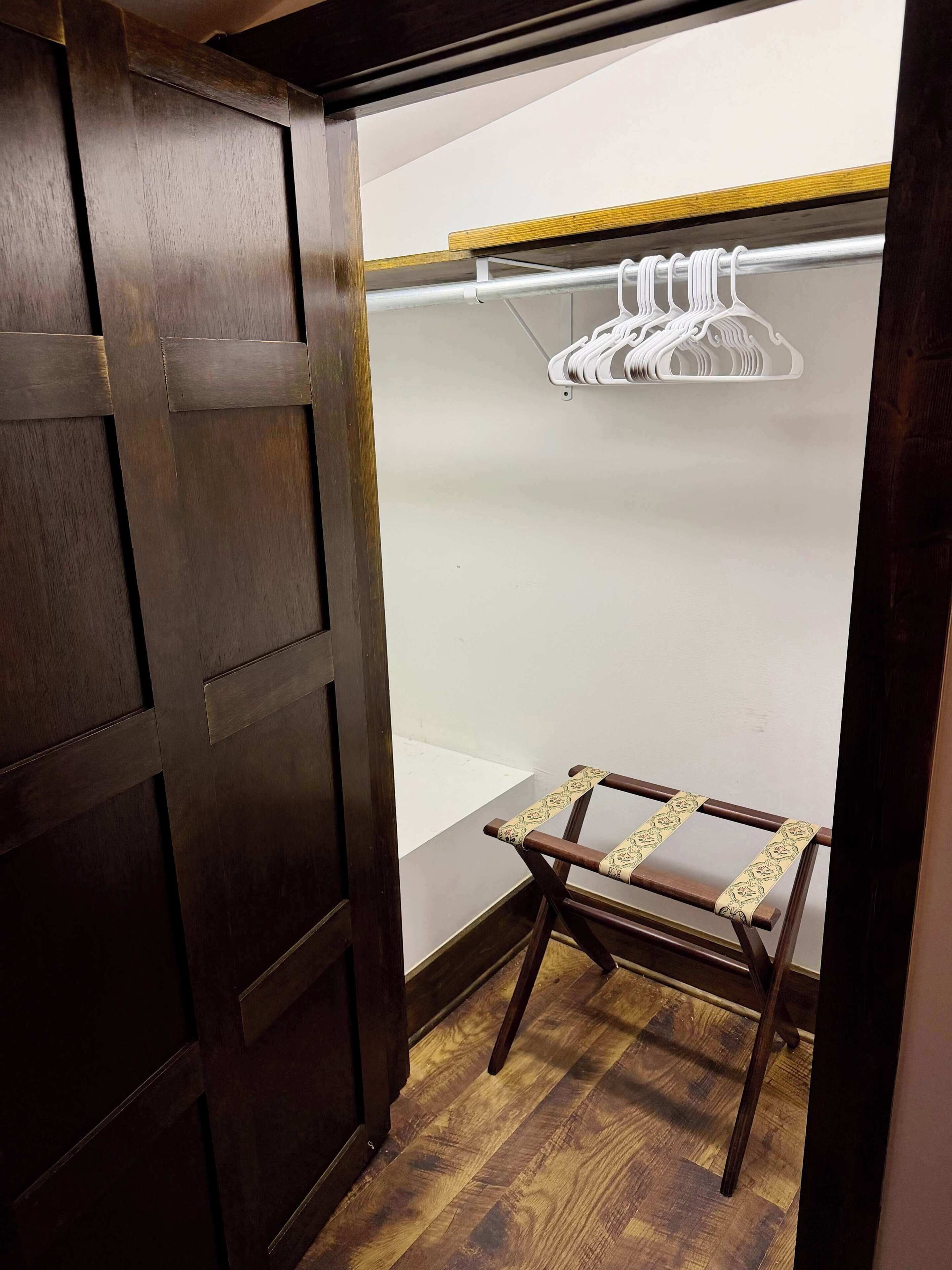 A wooden wardrobe with a mirror, a hanging clothes rack, and a small wooden table.